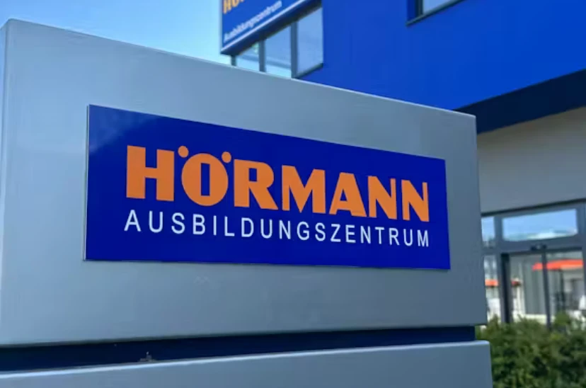 Firmenstele mit der Aufschrift Hörmann Ausbildungszentrum vor einem Gebäude